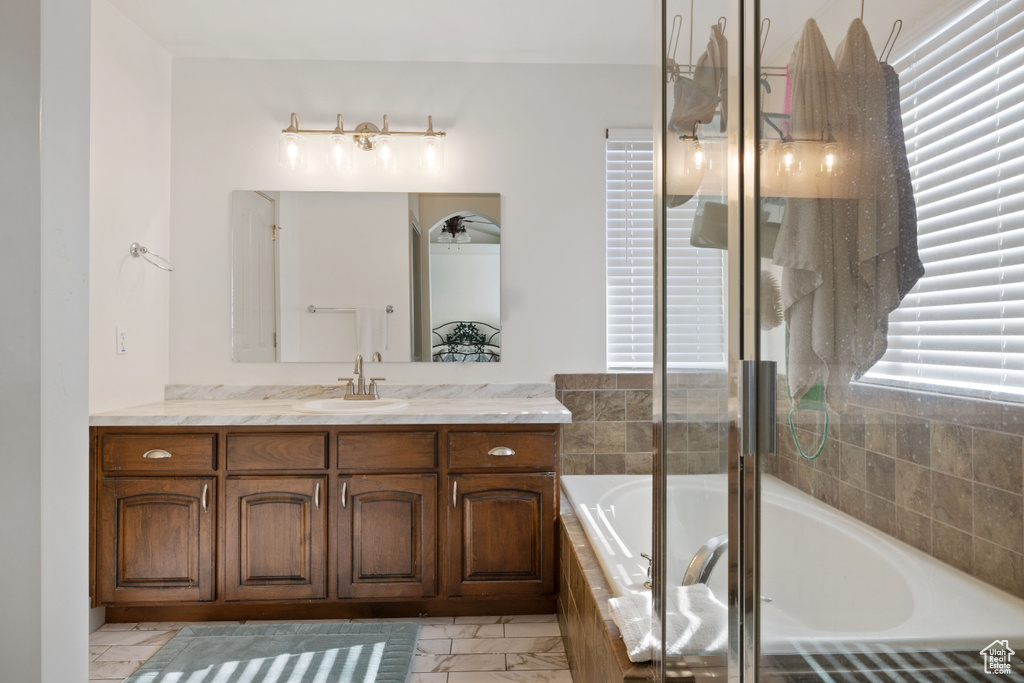 Bathroom featuring vanity, plenty of natural light, and a relaxing tiled tub