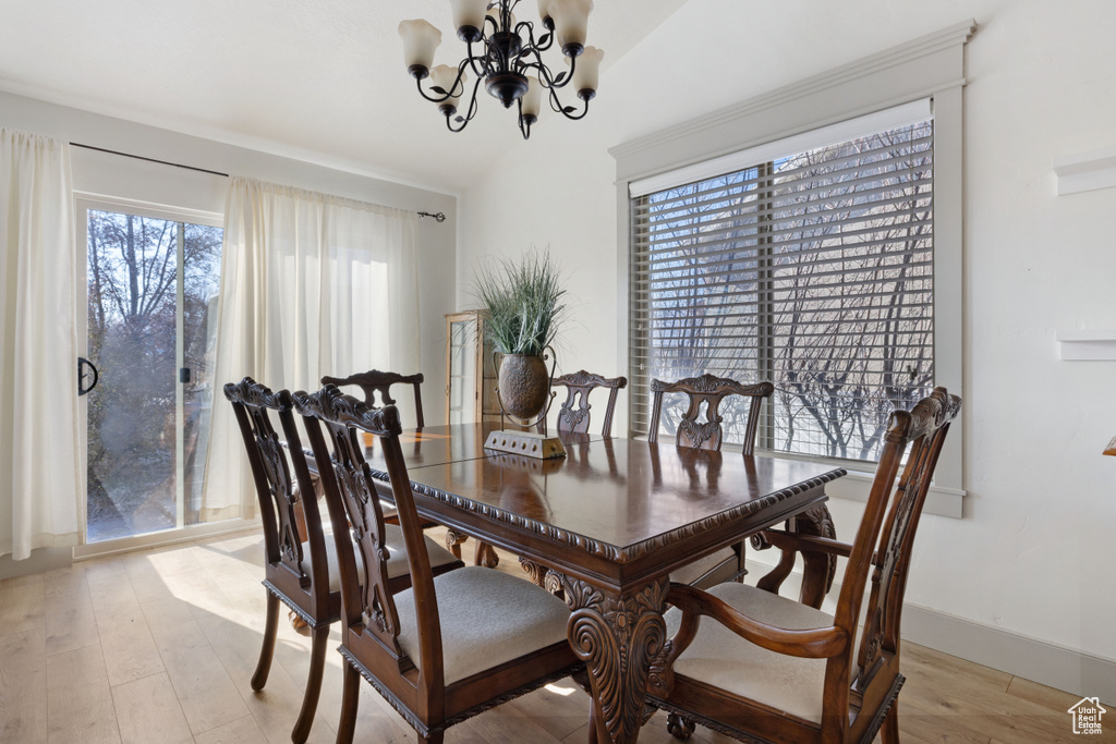 Dining area with a notable chandelier, vaulted ceiling, light hardwood / wood-style floors, and plenty of natural light