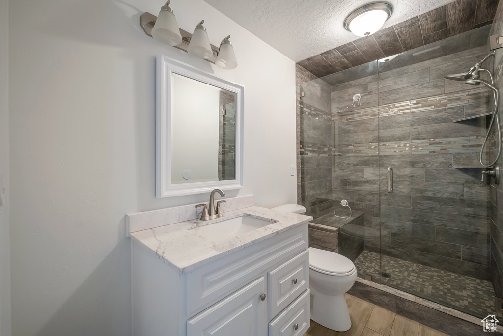Bathroom featuring toilet, vanity, a stall shower, and wood finished floors
