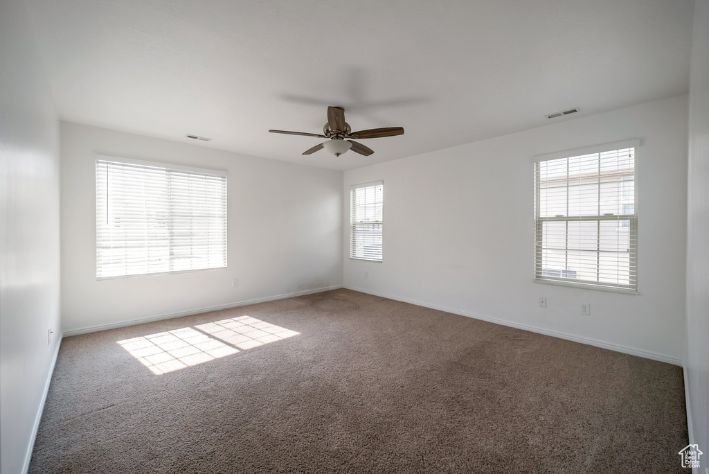 Carpeted empty room featuring a ceiling fan and baseboards