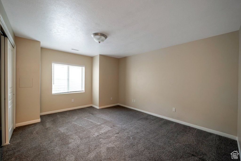 Spare room featuring dark colored carpet and baseboards