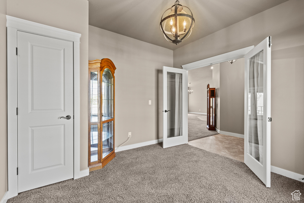 Unfurnished room featuring french doors, a chandelier, carpet, and baseboards