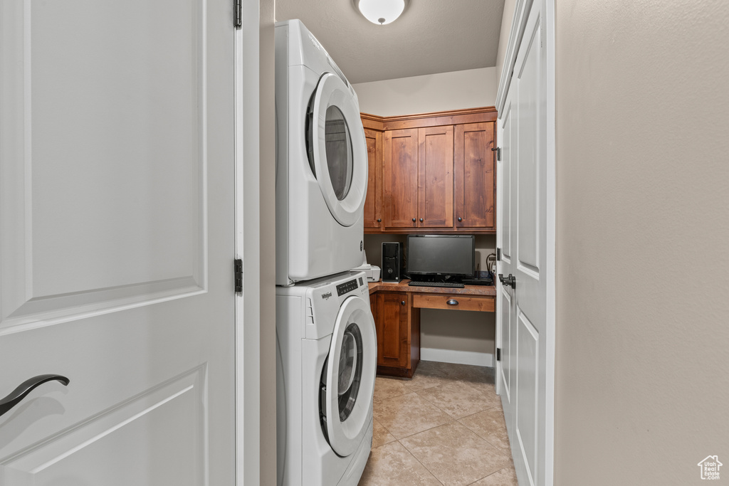 Laundry area with stacked washer / drying machine, cabinet space, and light tile patterned flooring