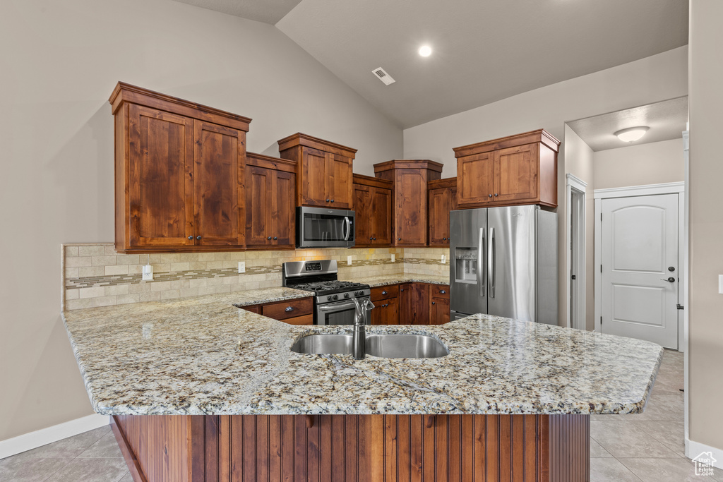 Kitchen with appliances with stainless steel finishes, a sink, a peninsula, light stone countertops, and vaulted ceiling