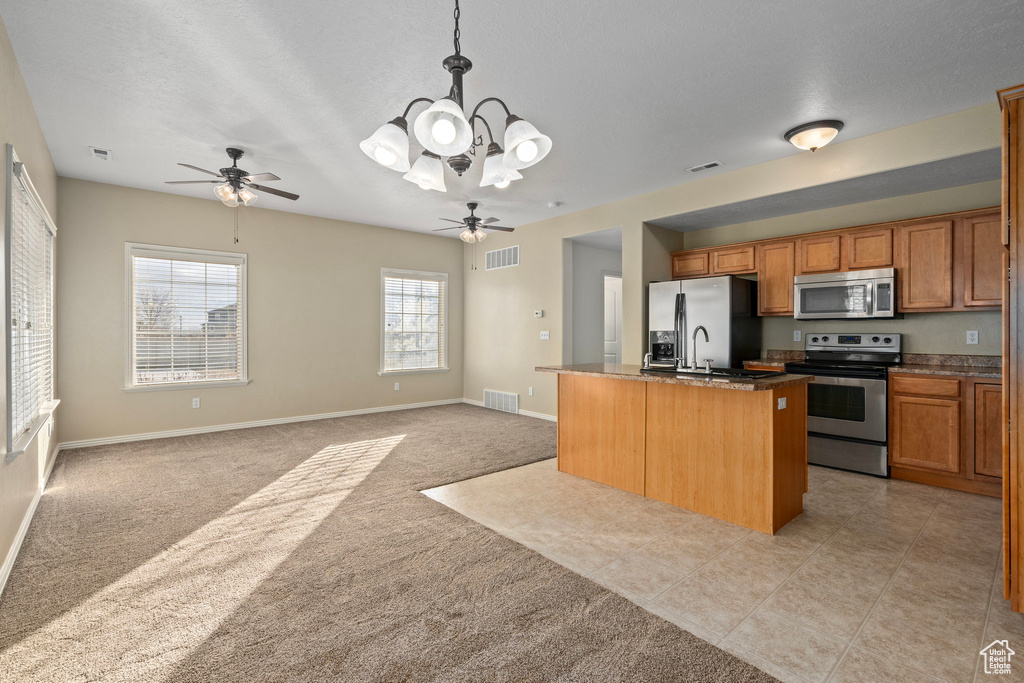 Kitchen featuring light carpet, an island with sink, pendant lighting, stainless steel appliances, and ceiling fan with notable chandelier