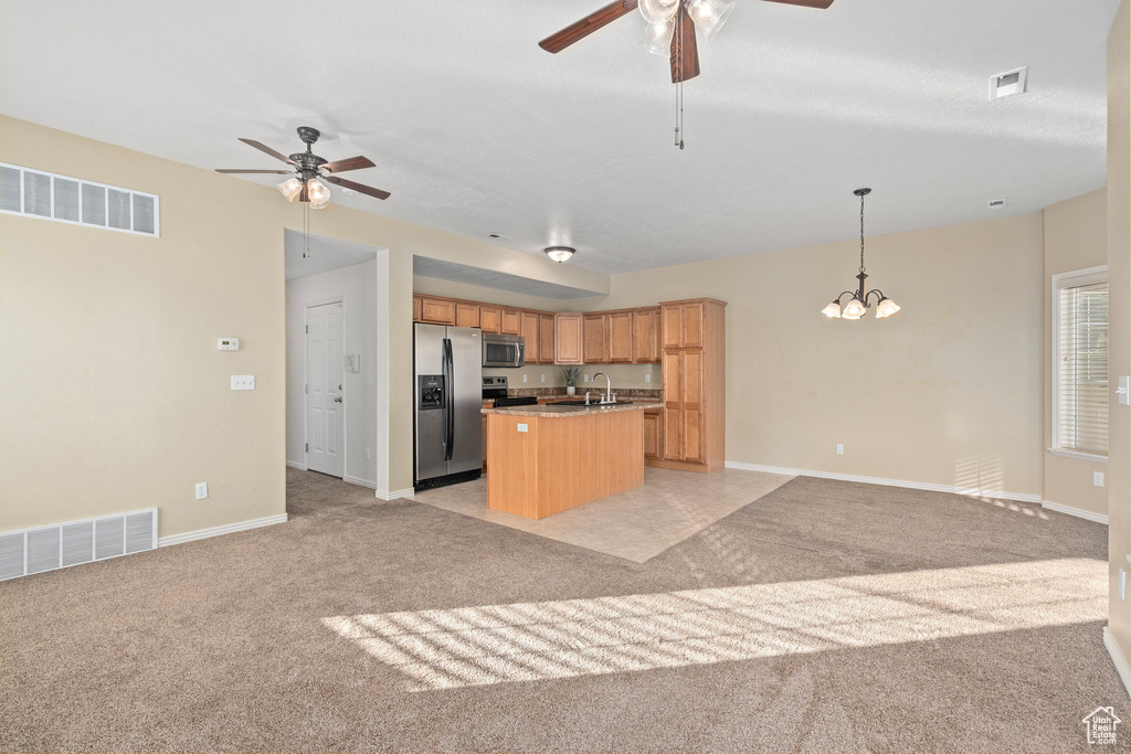 Kitchen featuring hanging light fixtures, a center island with sink, light colored carpet, stainless steel appliances, and ceiling fan with notable chandelier