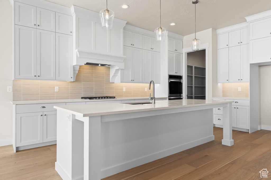 Kitchen featuring decorative light fixtures, stainless steel gas cooktop, a center island with sink, and white cabinets