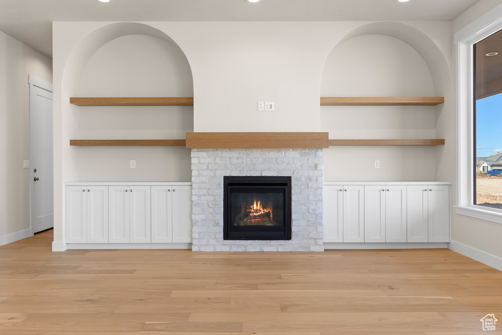 Unfurnished living room featuring a brick fireplace, light hardwood / wood-style flooring, and built in features