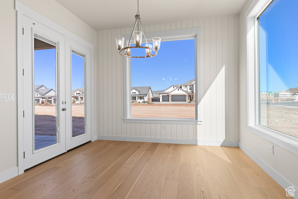 Unfurnished dining area with an inviting chandelier, french doors, and light wood-type flooring