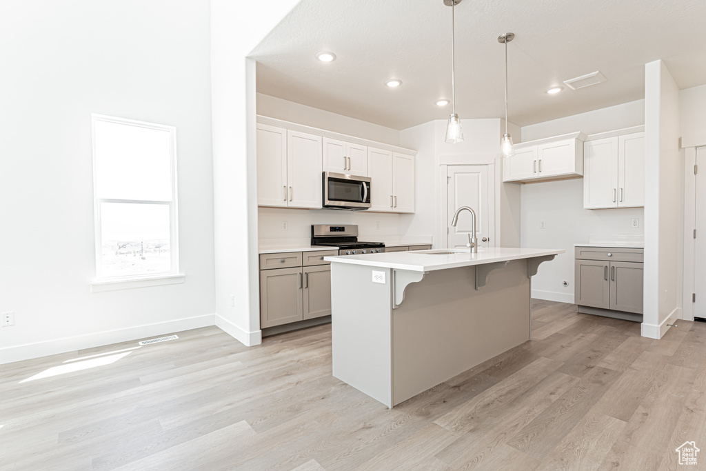 Kitchen with appliances with stainless steel finishes, a sink, light wood-style floors, a breakfast bar, and hanging light fixtures