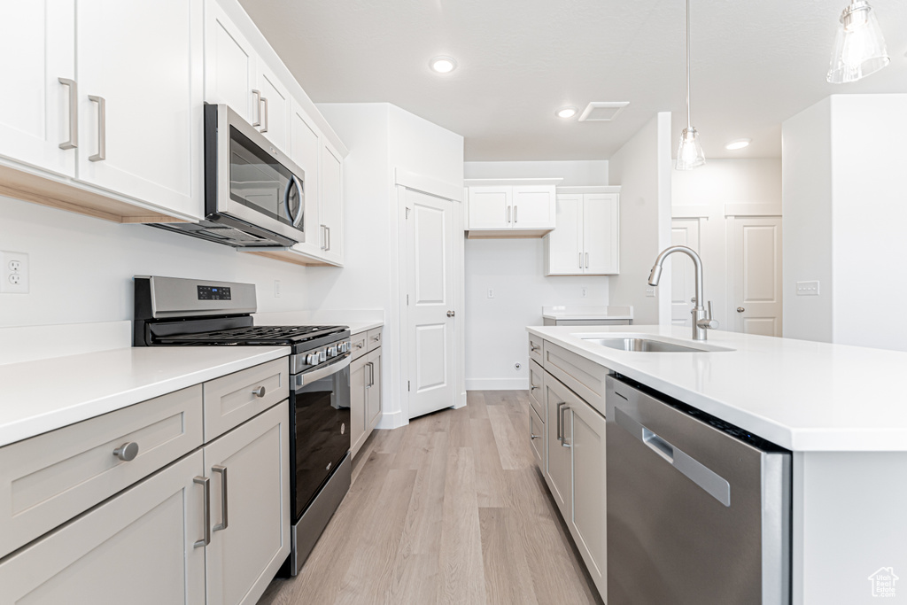 Kitchen with stainless steel appliances, a sink, light wood-style floors, light countertops, and recessed lighting