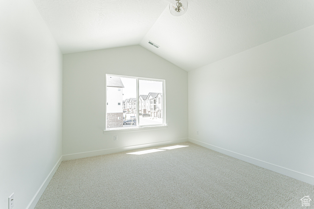 Carpeted spare room with vaulted ceiling and baseboards