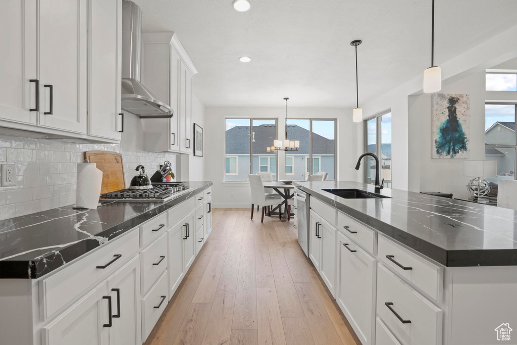 Kitchen featuring sink, hanging light fixtures, stainless steel appliances, a large island with sink, and wall chimney exhaust hood