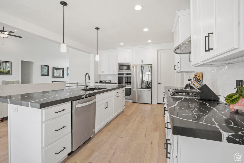 Kitchen featuring a kitchen island with sink, sink, stainless steel appliances, and white cabinets