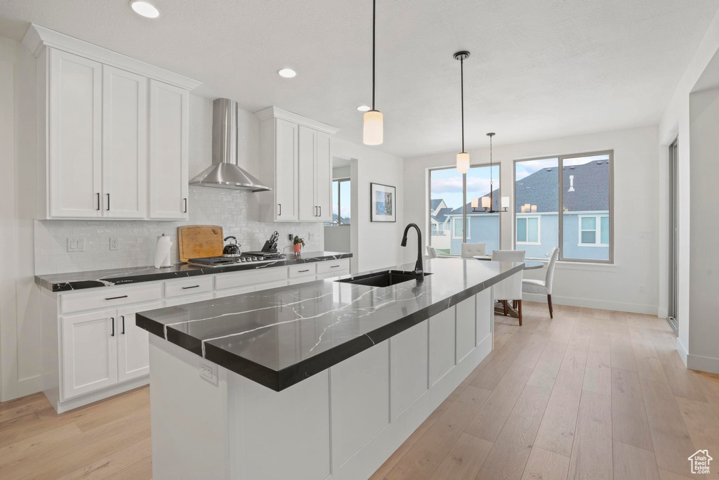 Kitchen with a kitchen island with sink, sink, white cabinets, and wall chimney exhaust hood