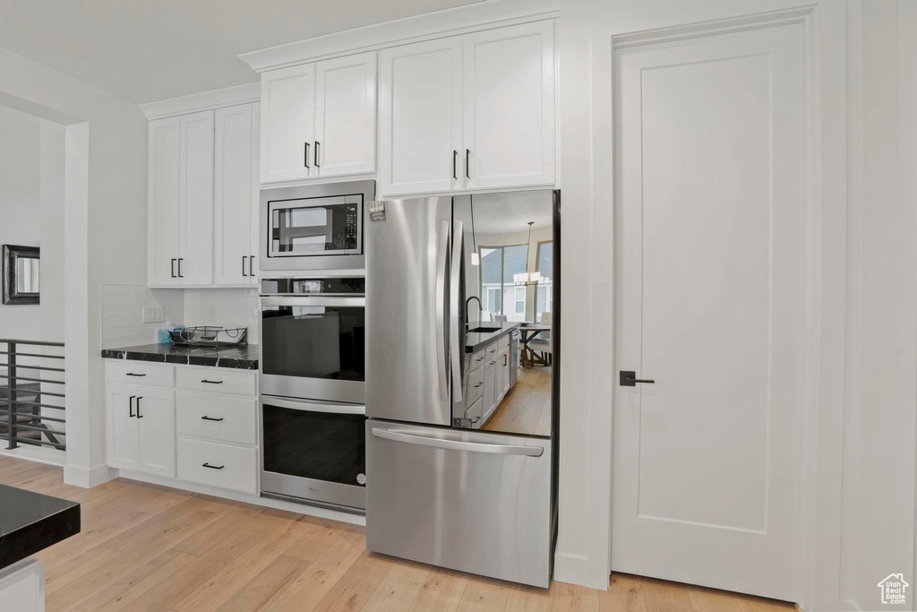 Kitchen with an inviting chandelier, light hardwood / wood-style floors, white cabinets, and appliances with stainless steel finishes