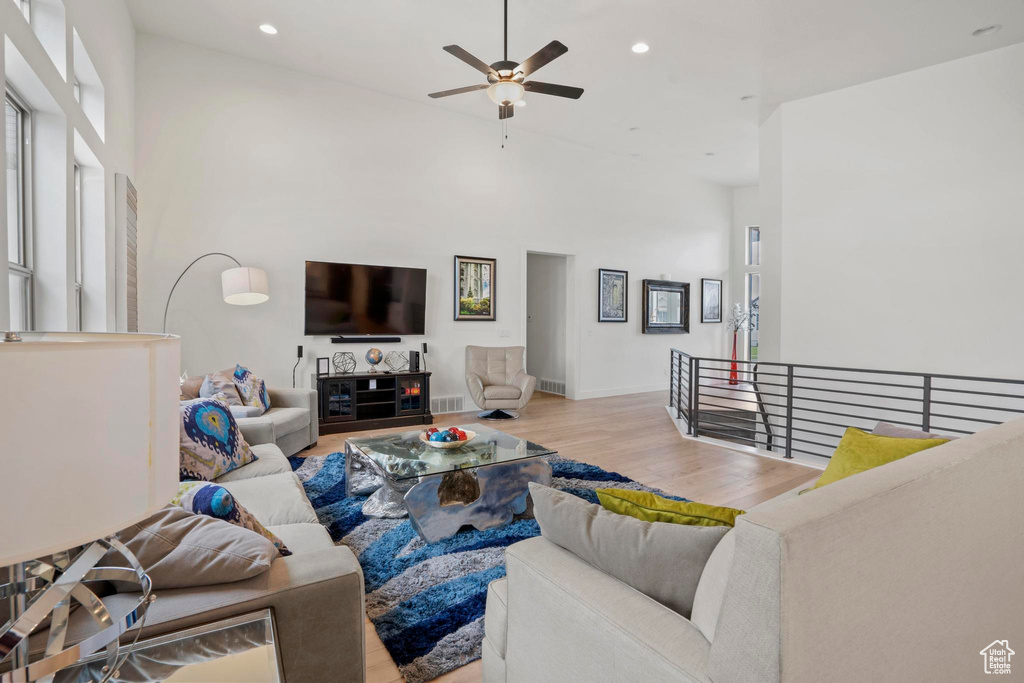 Living room with ceiling fan, a towering ceiling, and light hardwood / wood-style floors