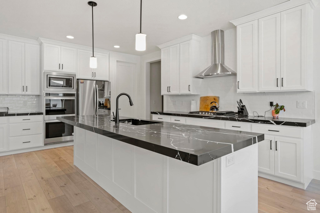 Kitchen with wall chimney exhaust hood, sink, hanging light fixtures, a center island with sink, and appliances with stainless steel finishes