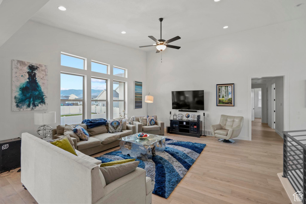 Living room with light hardwood / wood-style flooring, ceiling fan, and a high ceiling