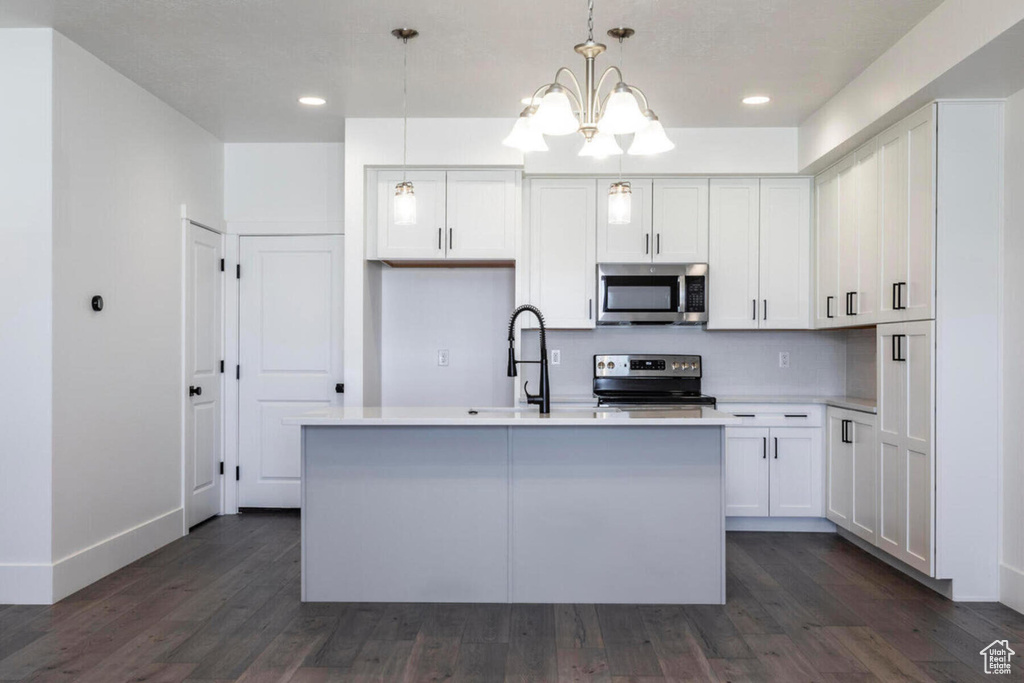 Kitchen with pendant lighting, dark wood-type flooring, appliances with stainless steel finishes, a kitchen island with sink, and white cabinets