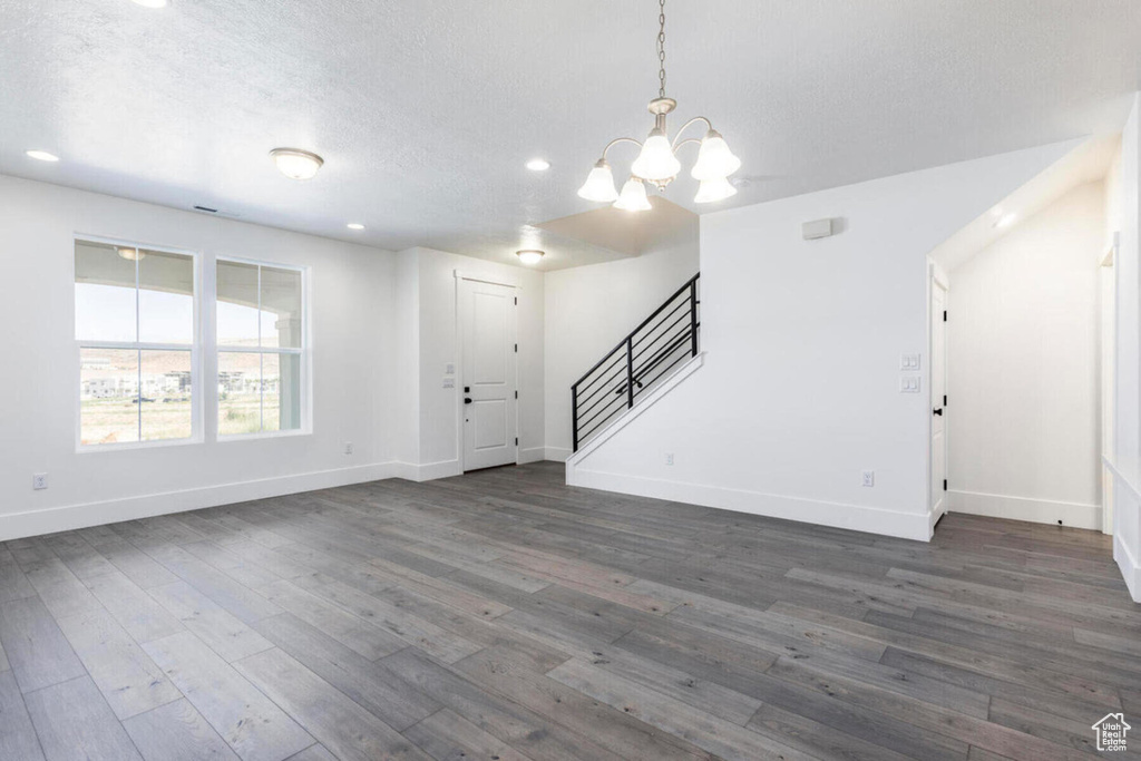 Unfurnished living room featuring a chandelier, dark hardwood / wood-style floors, and a textured ceiling