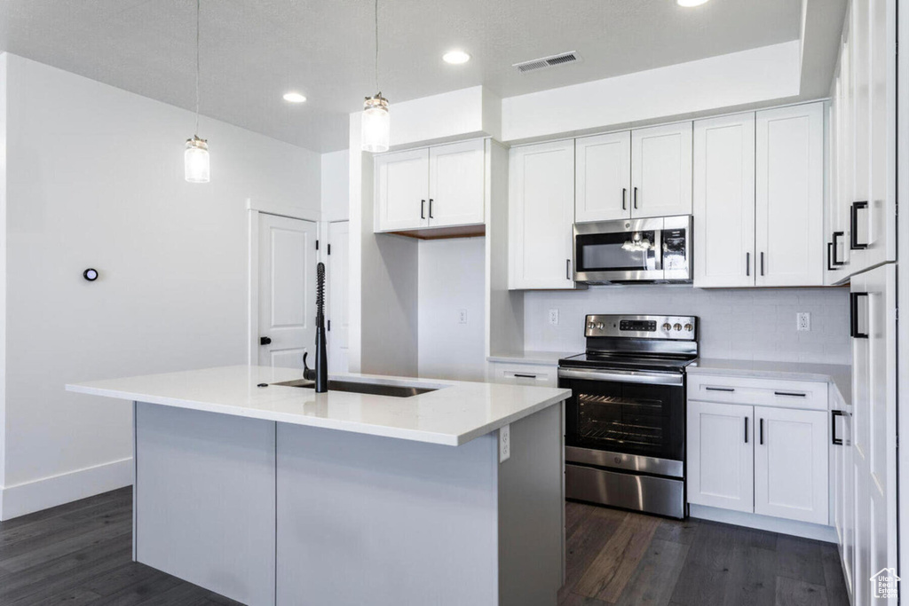 Kitchen featuring sink, stainless steel appliances, an island with sink, white cabinets, and decorative light fixtures