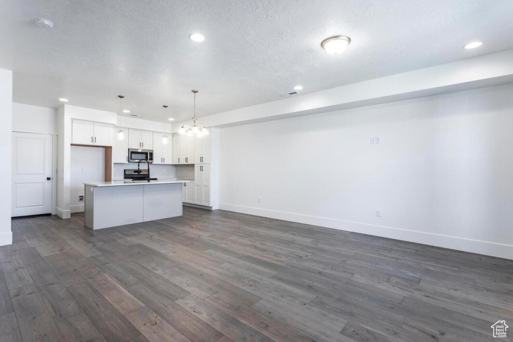 Kitchen featuring pendant lighting, white cabinetry, an island with sink, dark hardwood / wood-style flooring, and a textured ceiling