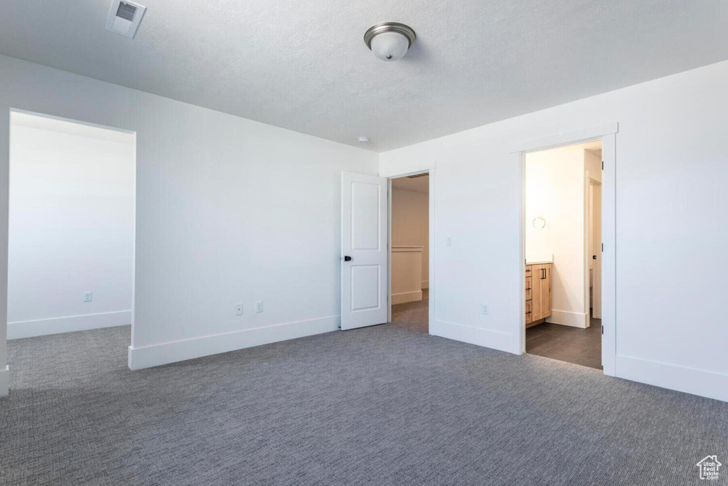 Unfurnished bedroom with a textured ceiling, dark carpet, and ensuite bath