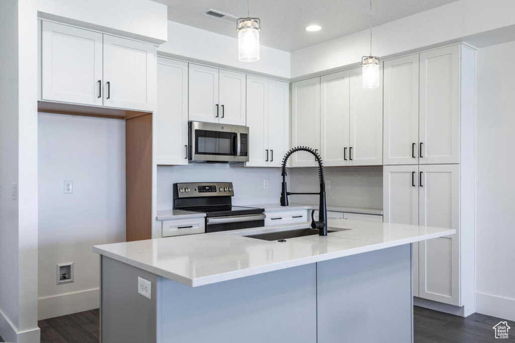 Kitchen with white cabinetry, appliances with stainless steel finishes, decorative light fixtures, and light stone countertops