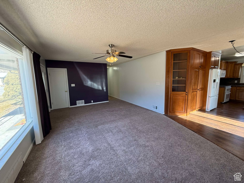 Unfurnished living room with a textured ceiling, ceiling fan, and dark colored carpet