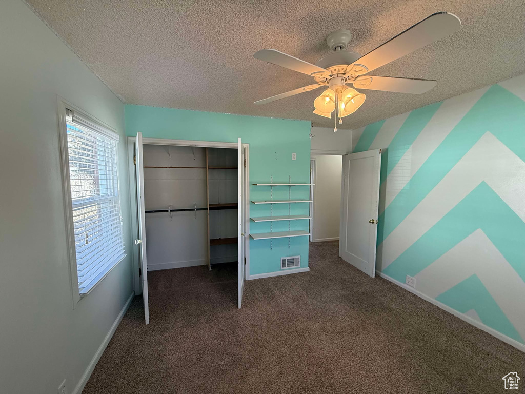 Unfurnished bedroom with a textured ceiling, a closet, ceiling fan, and dark colored carpet