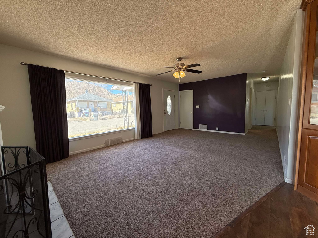 Unfurnished living room featuring ceiling fan, dark carpet, and a textured ceiling