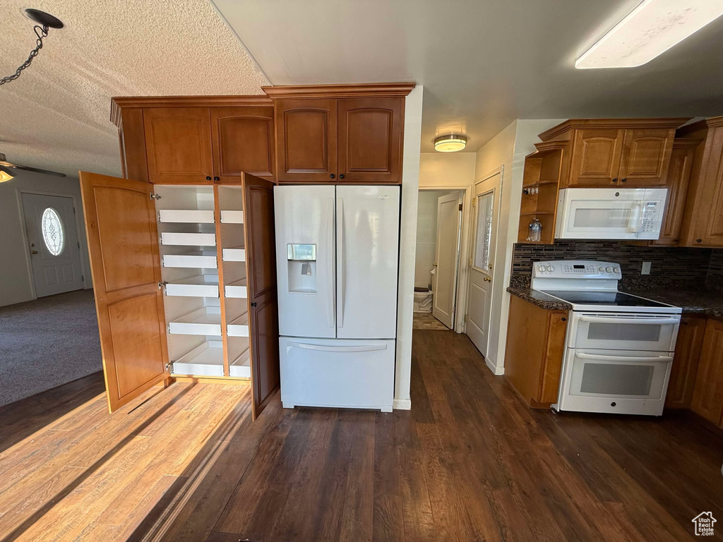 Kitchen featuring white appliances, dark wood-type flooring, decorative backsplash, and dark stone counters