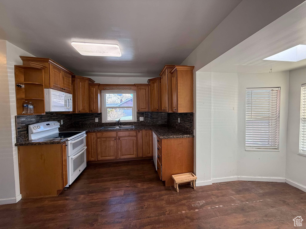 Kitchen with dark wood-type flooring, sink, a skylight, white appliances, and decorative backsplash