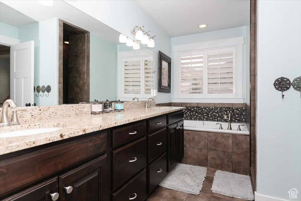 Bathroom with tile patterned flooring, tiled tub, and vanity