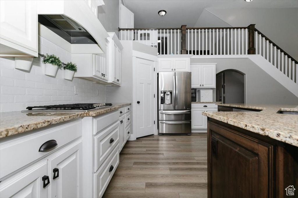 Kitchen with white cabinetry, appliances with stainless steel finishes, light stone countertops, and hardwood / wood-style floors