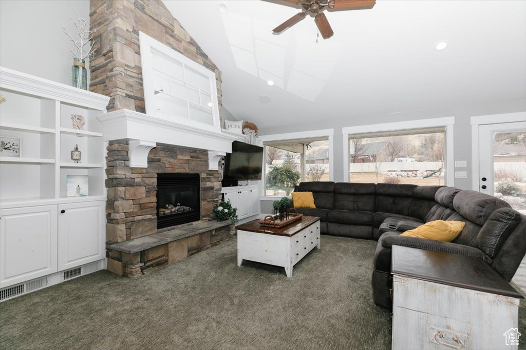 Living room with ceiling fan, a stone fireplace, high vaulted ceiling, and dark carpet