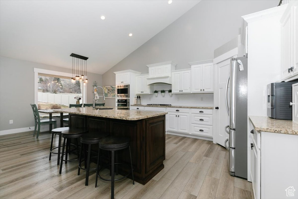 Kitchen with sink, stainless steel appliances, an island with sink, white cabinets, and decorative light fixtures