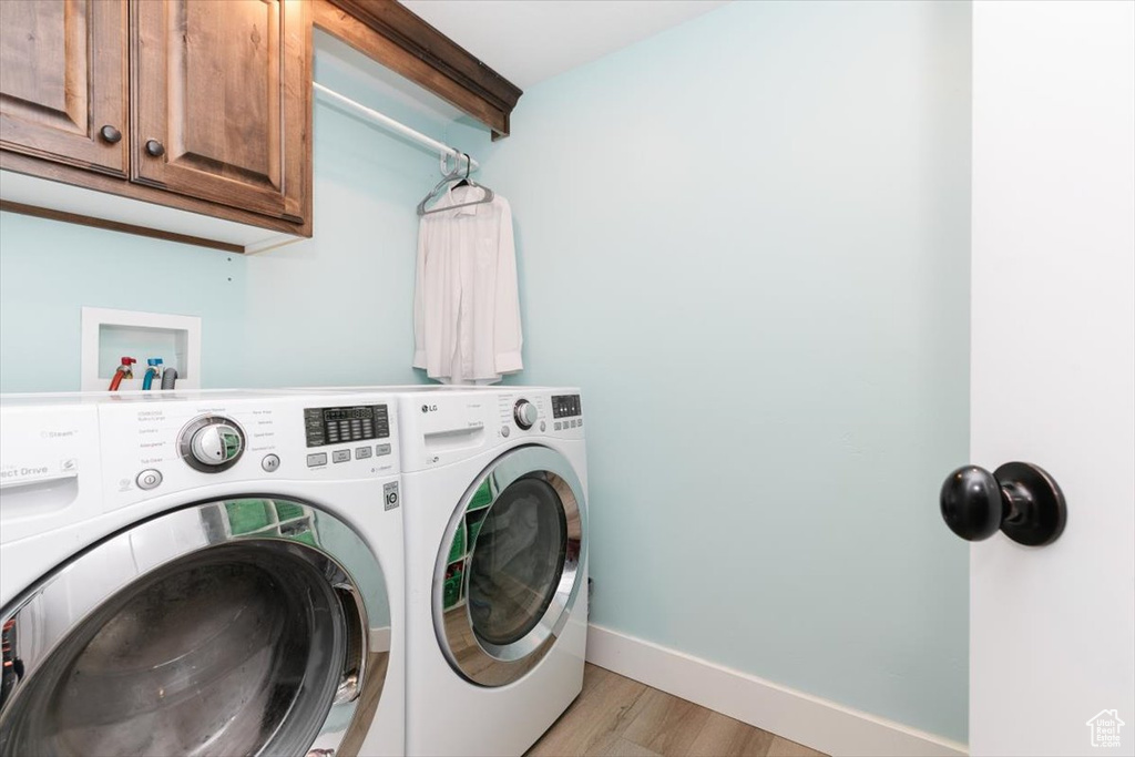 Laundry room featuring light hardwood / wood-style floors, cabinets, and washing machine and clothes dryer