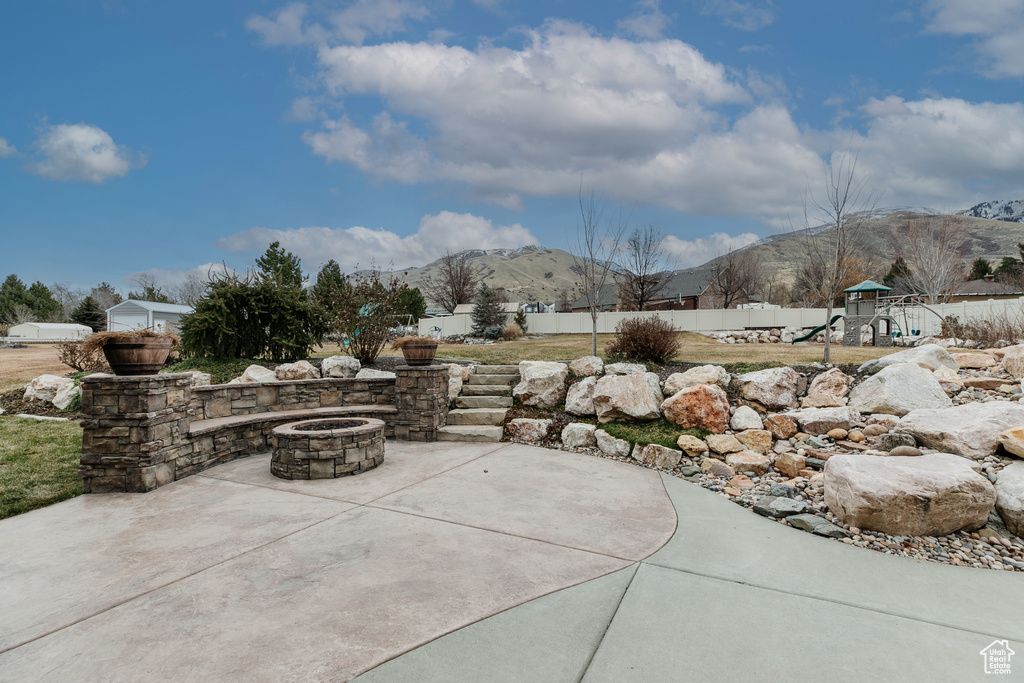 View of patio with a playground, a mountain view, and a fire pit