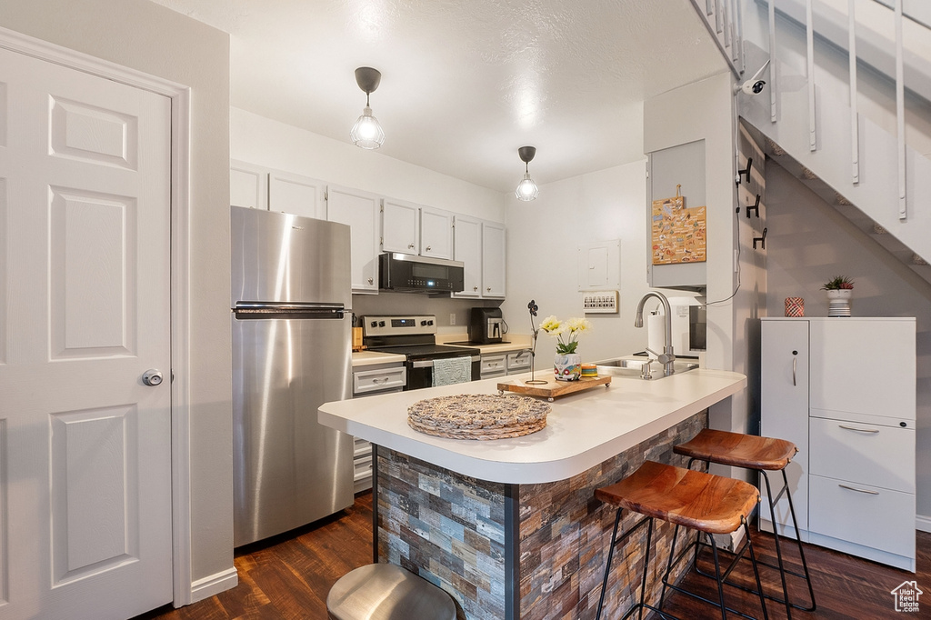 Kitchen with white cabinetry, sink, a kitchen bar, hanging light fixtures, and stainless steel appliances