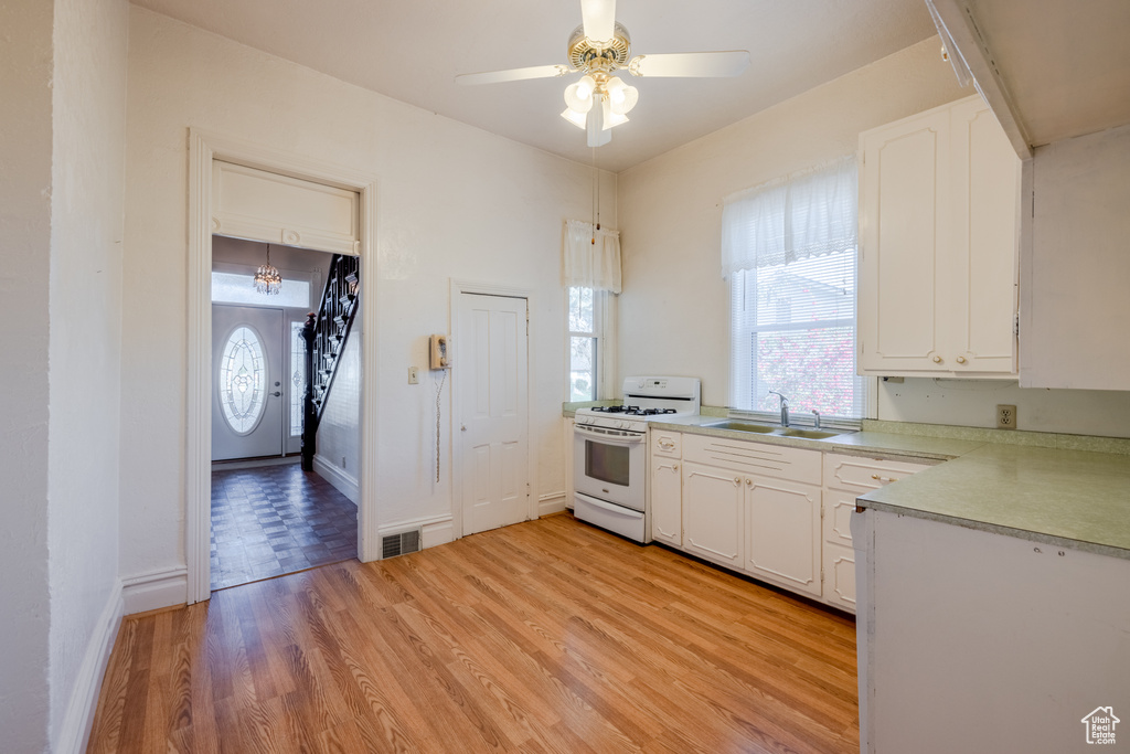 Kitchen featuring white range with gas cooktop, sink, white cabinetry, and light wood-type flooring