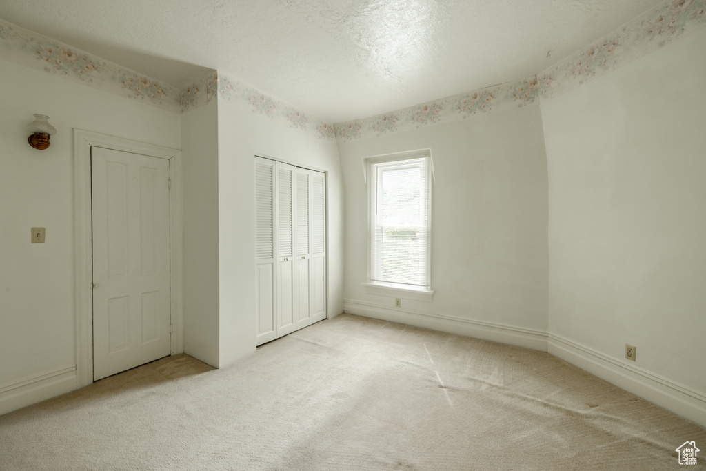 Unfurnished bedroom with light colored carpet, a textured ceiling, and a closet