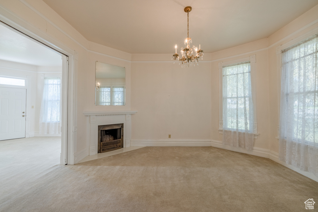 Unfurnished living room with an inviting chandelier, carpet floors, and a healthy amount of sunlight