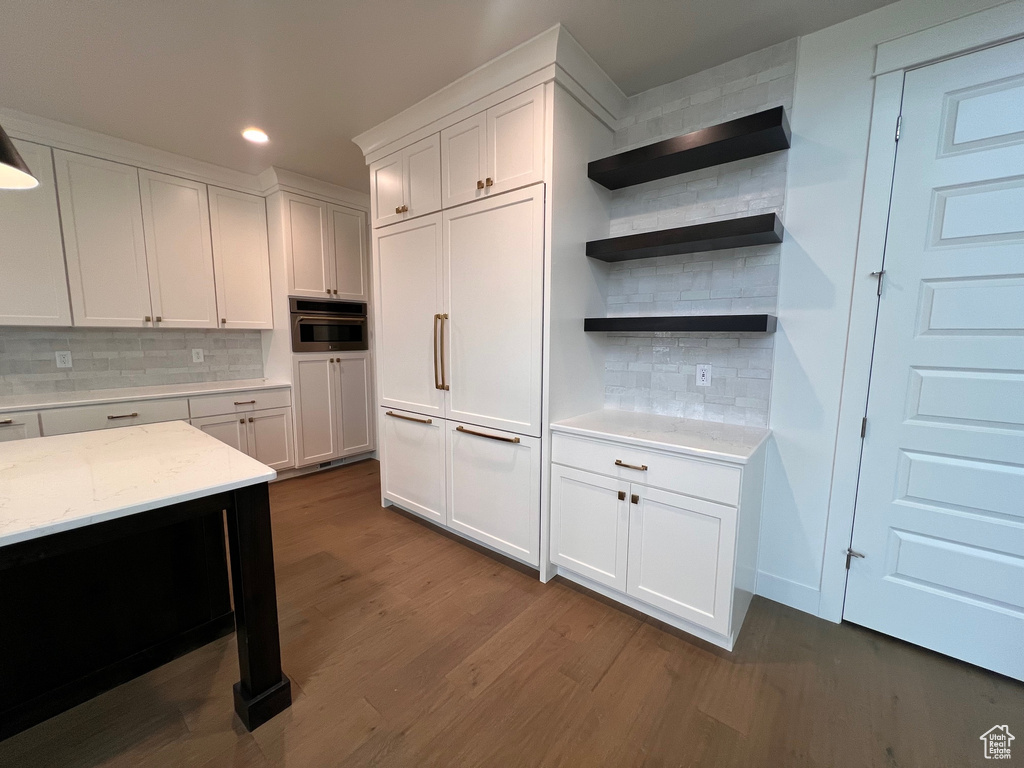 Kitchen with dark hardwood / wood-style floors, tasteful backsplash, white cabinets, stainless steel oven, and light stone countertops