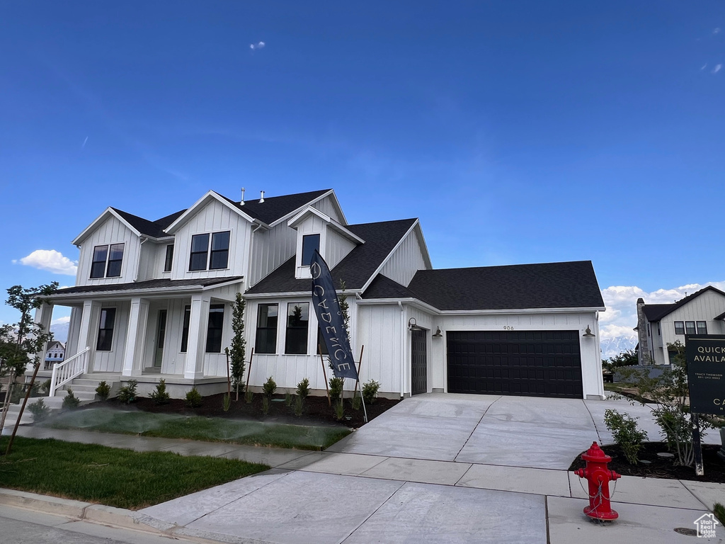 Modern inspired farmhouse featuring an attached garage, covered porch, driveway, board and batten siding, and roof with shingles