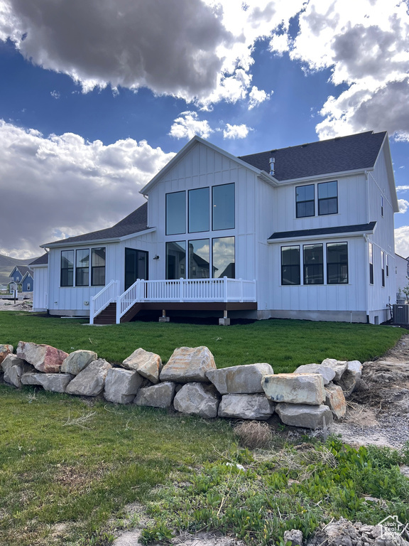 Back of property featuring board and batten siding, cooling unit, a yard, and a shingled roof