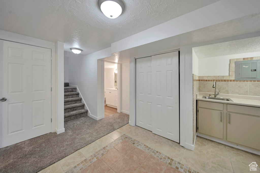 Basement with sink, light colored carpet, electric panel, and a textured ceiling