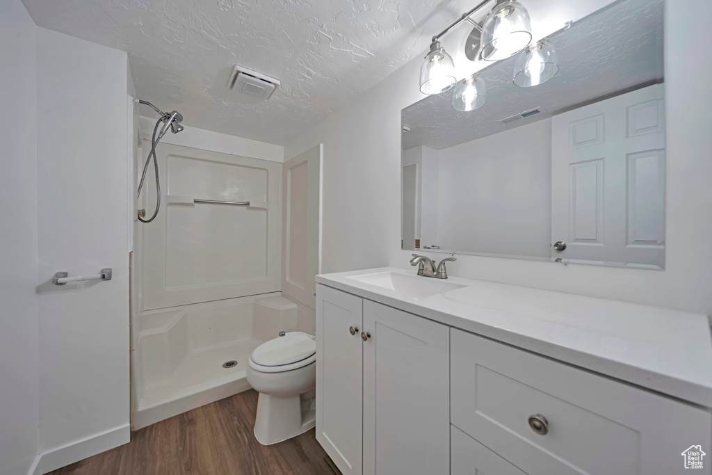 Bathroom featuring a shower, hardwood / wood-style flooring, vanity, toilet, and a textured ceiling
