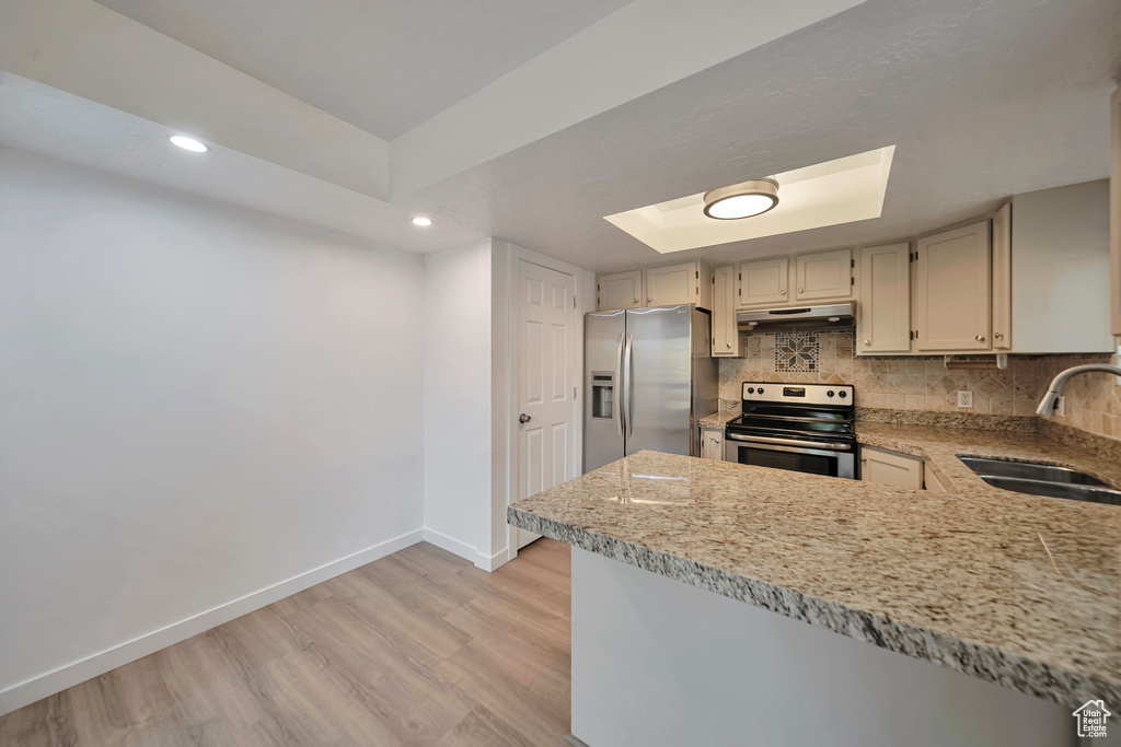 Kitchen featuring appliances with stainless steel finishes, sink, decorative backsplash, a raised ceiling, and light hardwood / wood-style flooring